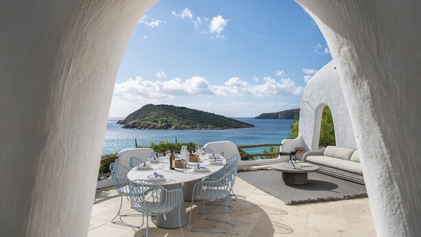 An outdoor dining area with a table set for four, overlooking a coastal landscape with a small island and the sea. - The Icon - Tuerredda (Teulada)