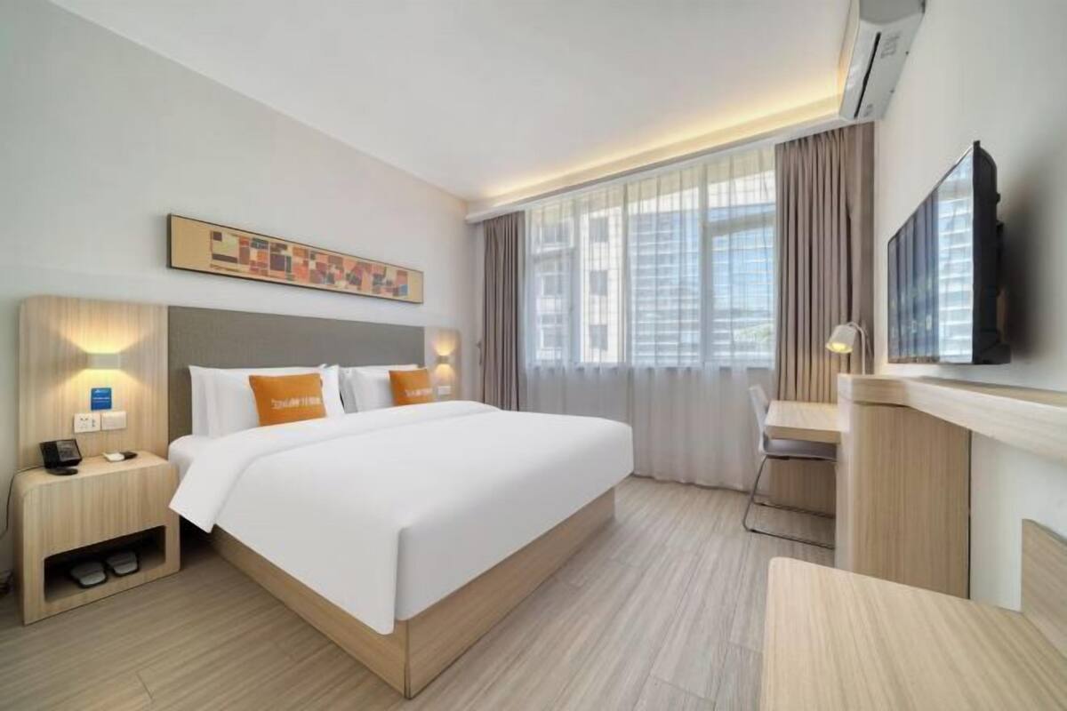 A hotel room with a large bed, a desk, a chair, a TV, and a window with curtains.