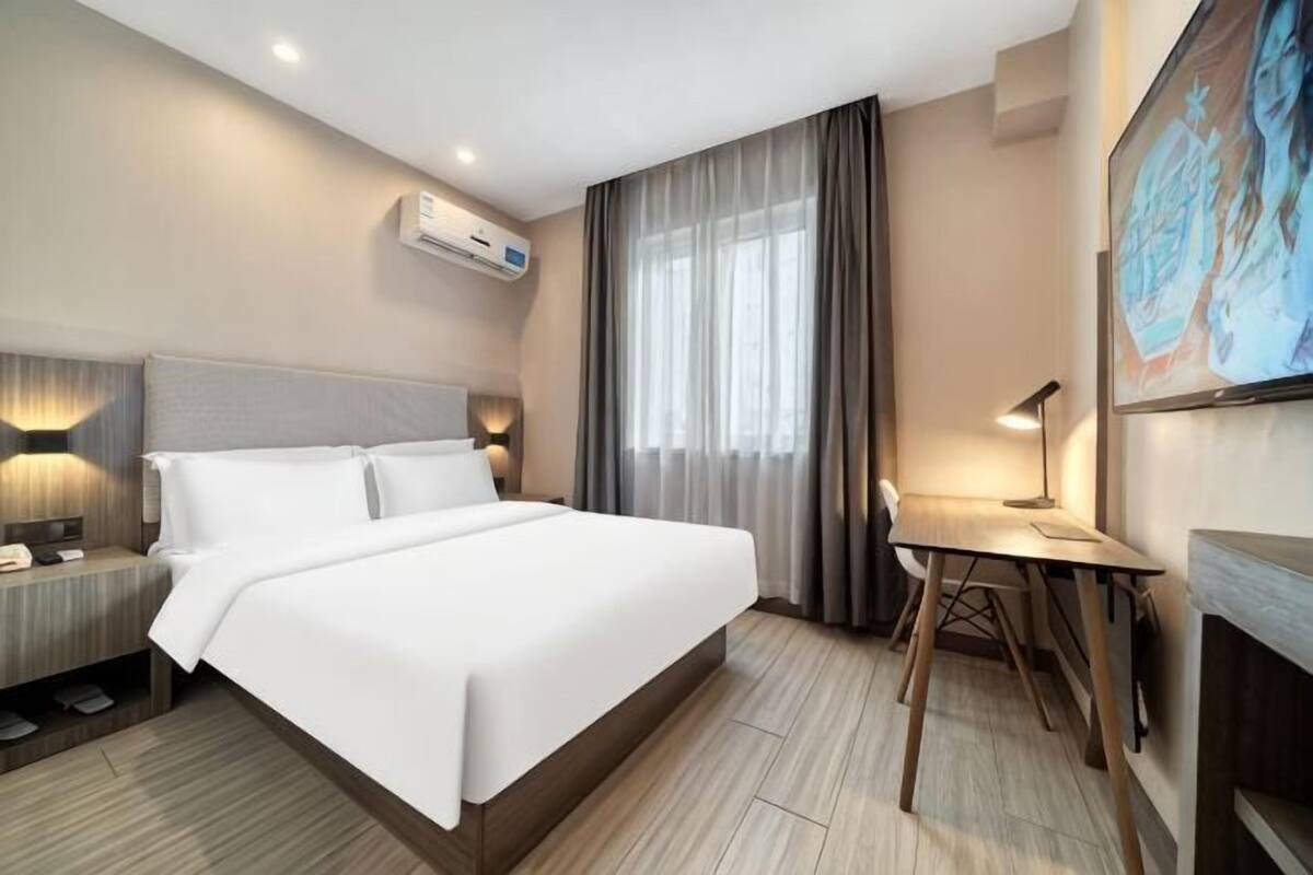A hotel room with a large bed, bedside tables, a desk, and a fireplace.