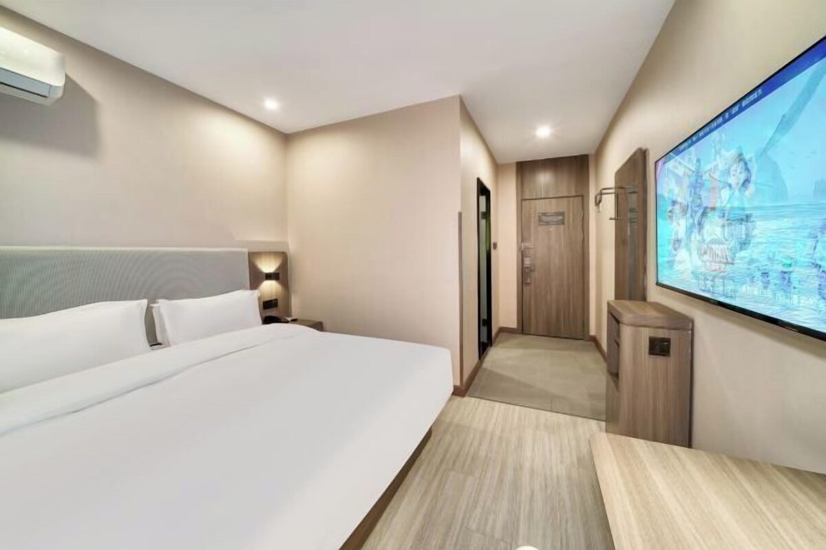 A hotel room with a large bed, a TV mounted on the wall, and a wooden desk.