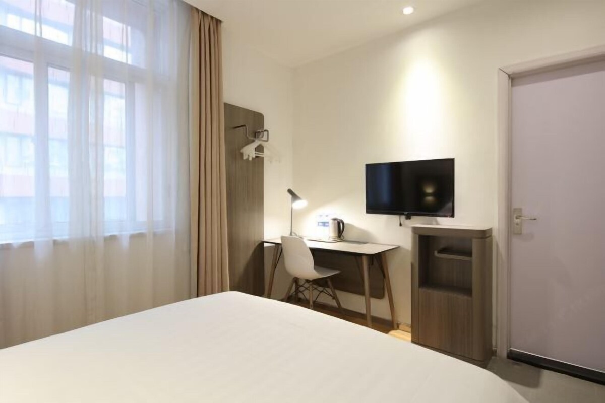 A hotel room with a bed, a desk with a chair, a television, and a door.
