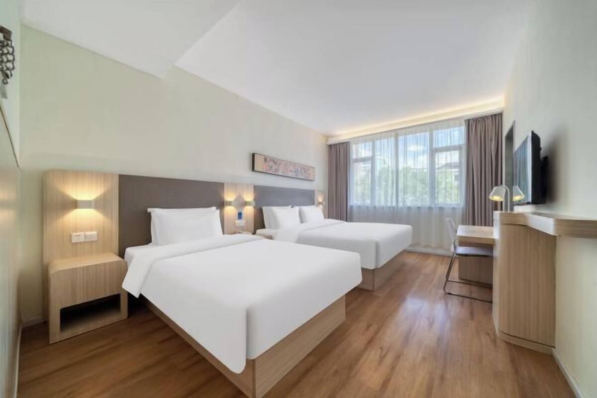 A hotel room with two beds, a desk, and a TV.