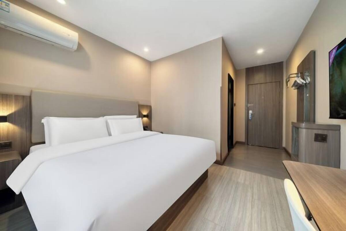 A modern hotel room with a large bed, a desk, and a TV.