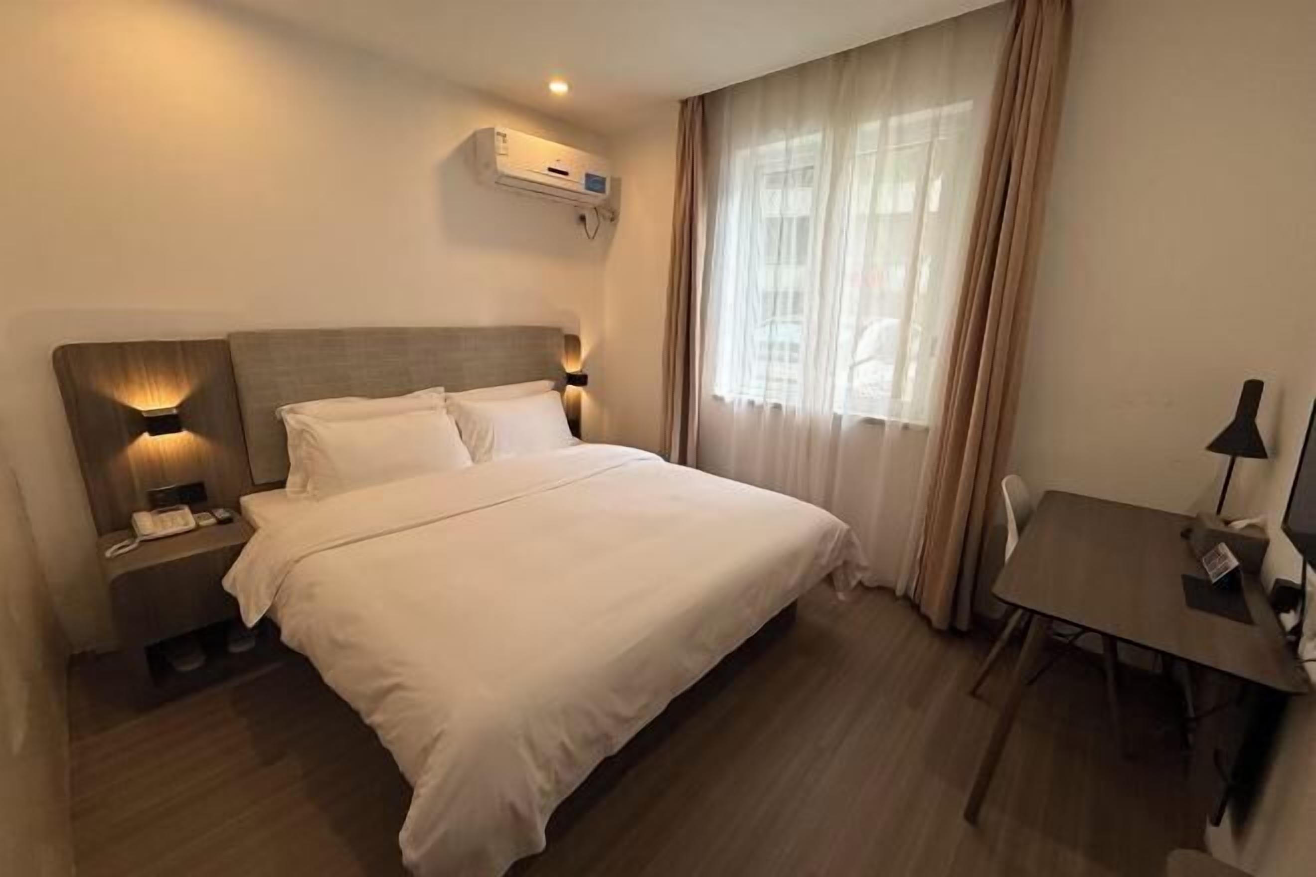 Een hotelkamer met een bed, nachtlampjes, een bureau en een raam met gordijnen.
