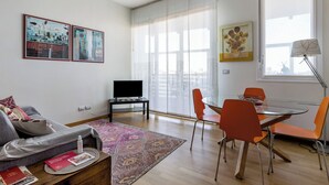 A modern living room with a sofa, a glass dining table with orange chairs, a TV on a stand, and artwork on the walls. - Una terrazza sulla città by Wonderful Italy (Bologna)