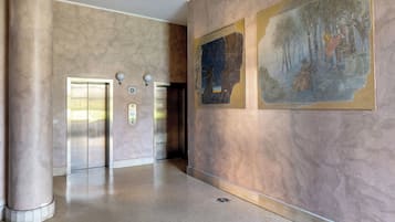 Un hall d’entrée spacieux aux murs de marbre, doté de deux ascenseurs et orné d’une grande fresque murale.