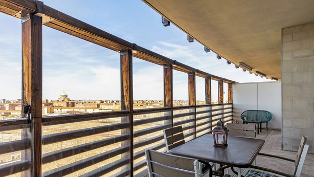 A balcony with a view of a cityscape, featuring a wooden railing, a table with chairs, and a lantern. - Una terrazza sulla città by Wonderful Italy (Bologna)
