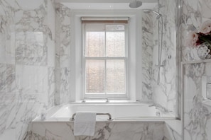 A bathroom with a marble wall, a window, a shower, and a bathtub.