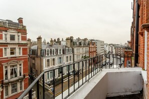 Une vue depuis un balcon donnant sur une rue bordée de bâtiments historiques, avec un ciel dégagé et un piéton.