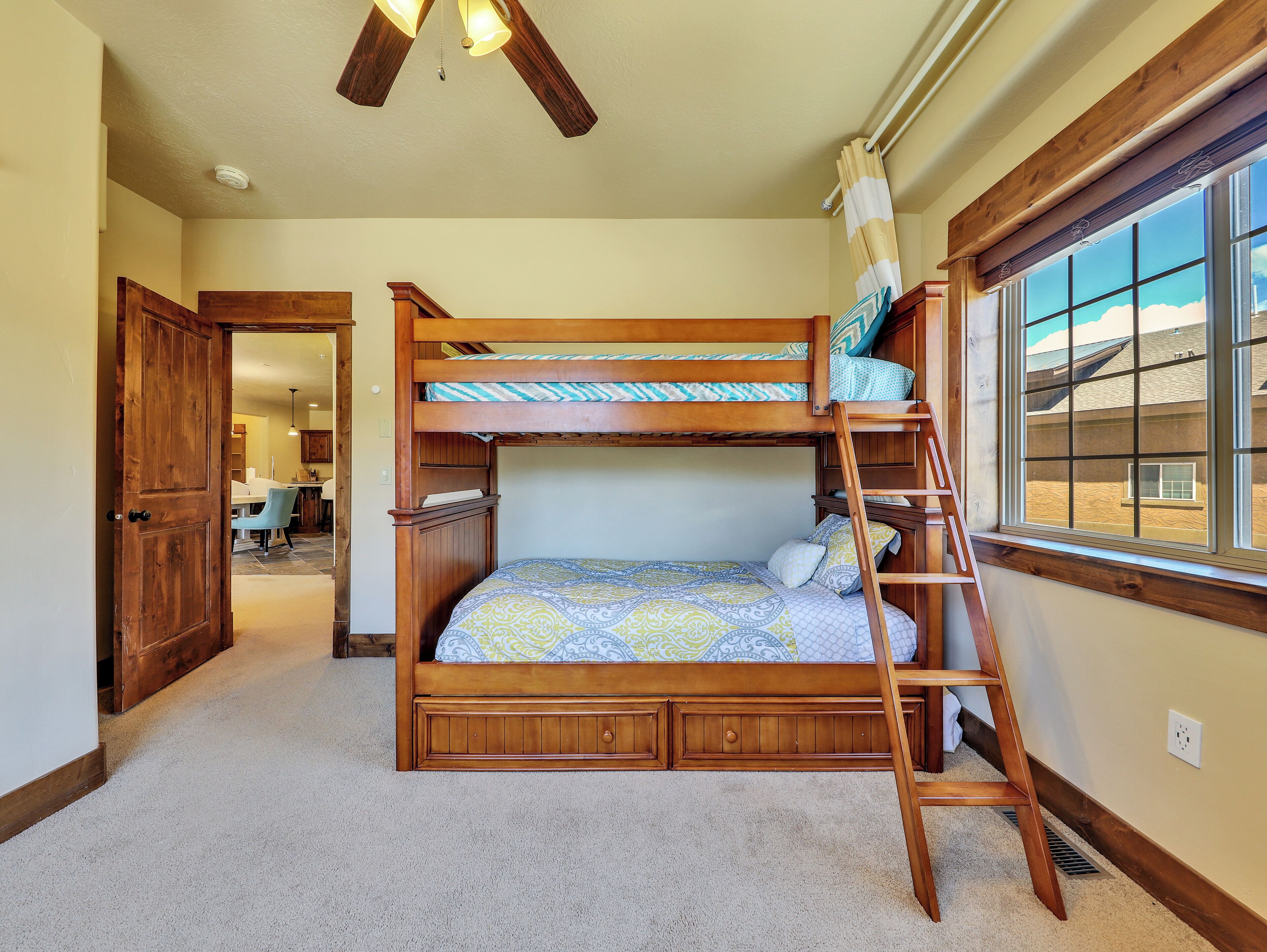 A bunk bed with a ladder, a window with a view, and a door leading to a kitchen area.
