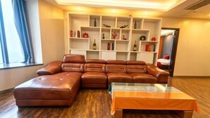 Ein Wohnzimmer mit einem braunen Ledersofa, einem Glastisch und einer weißen Regaleinheit mit verschiedenen Dekorationsobjekten.