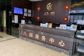 A reception desk with a sign indicating a business center, a computer, and a monitor. - Bamin Hotel (Lai'an)