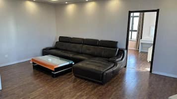Una sala de estar con un sofá modular, una mesa de centro de vidrio y piso de madera.