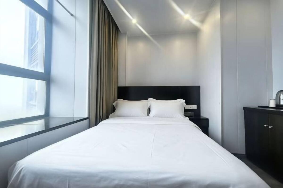 Une chambre d’hôtel avec un grand lit, une table de chevet, une commode et une fenêtre avec des rideaux.