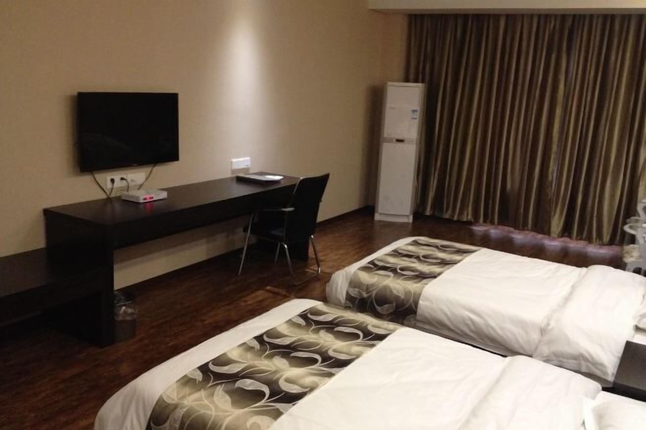 Quarto de hotel com duas camas, uma escrivaninha, uma cadeira, uma televisão e um mini-bar.