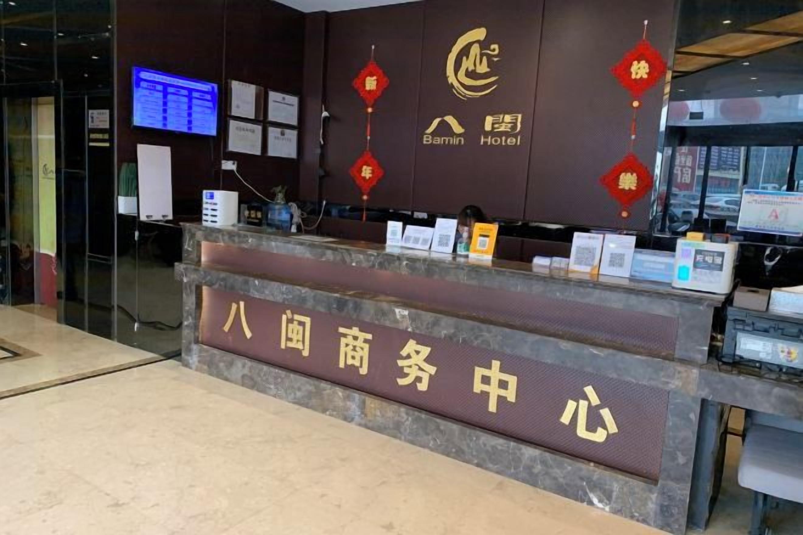 A hotel reception desk with a digital display, a signboard, and a counter with various items.