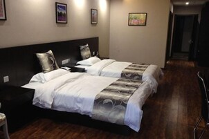 Una habitación de hotel con dos camas, un cabecero oscuro, una mesita de noche pequeña y una silla.