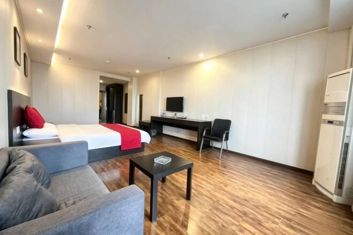 Quarto de hotel com cama, escrivaninha, cadeira, sofá e uma mesinha.