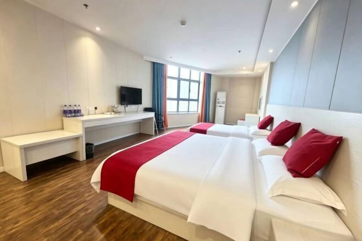 Une chambre d’hôtel avec deux lits, un bureau doté d’un téléviseur à écran plat, un banc et une fenêtre avec des rideaux.