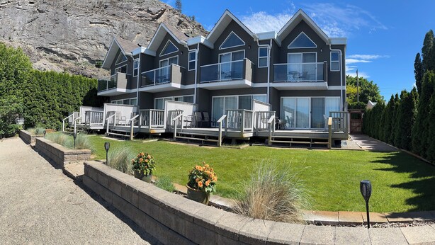 A multi-story house with a balcony, a driveway, and a mountain backdrop.