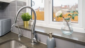 A kitchen with a stainless steel sink, a potted plant, and a vase with a flower on the windowsill. - Beautiful 4 Bedroom House Immaculate Condition. Just Refurbished House. (Romford)