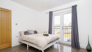 A bedroom with a bed, a wooden door, a window with curtains, and a view of the outside. - Beautiful 4 Bedroom House Immaculate Condition. Just Refurbished House. (Romford)