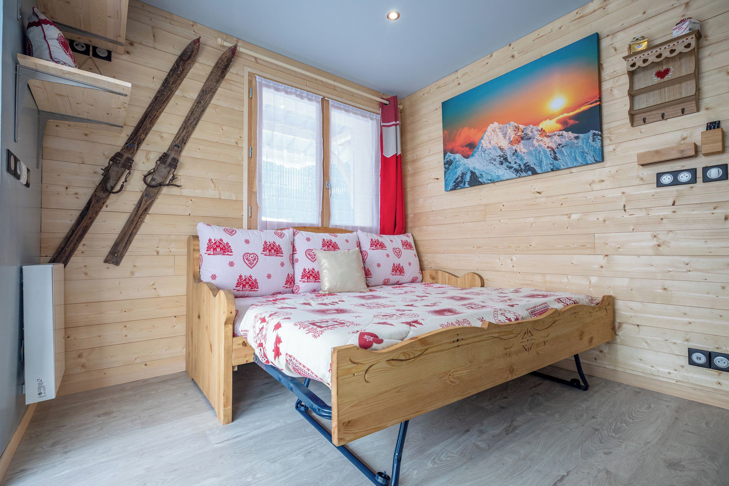 A wooden room with a bed, a window, a painting, and a ski rack.