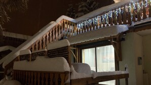 Eine mit Schnee bedeckte Holztreppe führt zu einem Balkon mit Lichterketten.