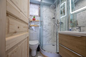 Ett badrum med en dusch som är avskärmad med glasväggar, en toalett och en tvättställsmöbel med en spegel.