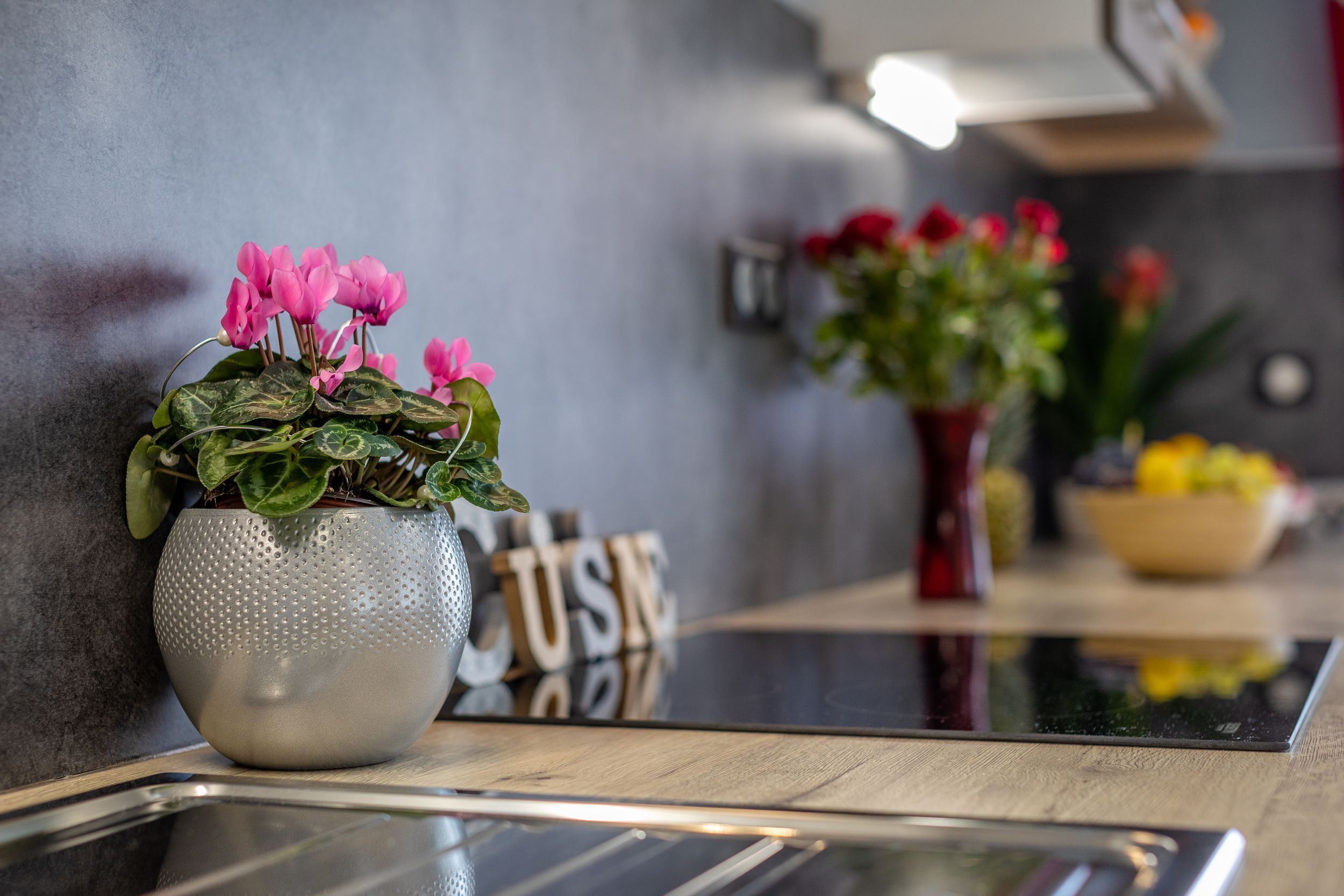 Een moderne keuken met een glanzend aanrecht, een potplant met roze bloemen en een decoratief bord met de tekst 