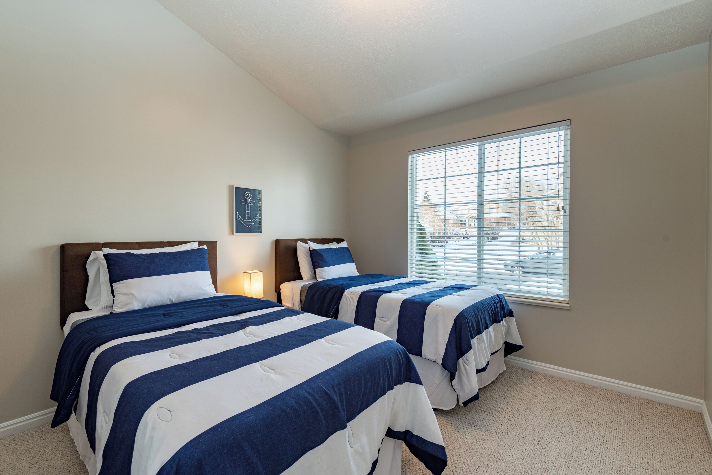 A bedroom with two beds, a window with blinds, and a small wall-mounted artwork.