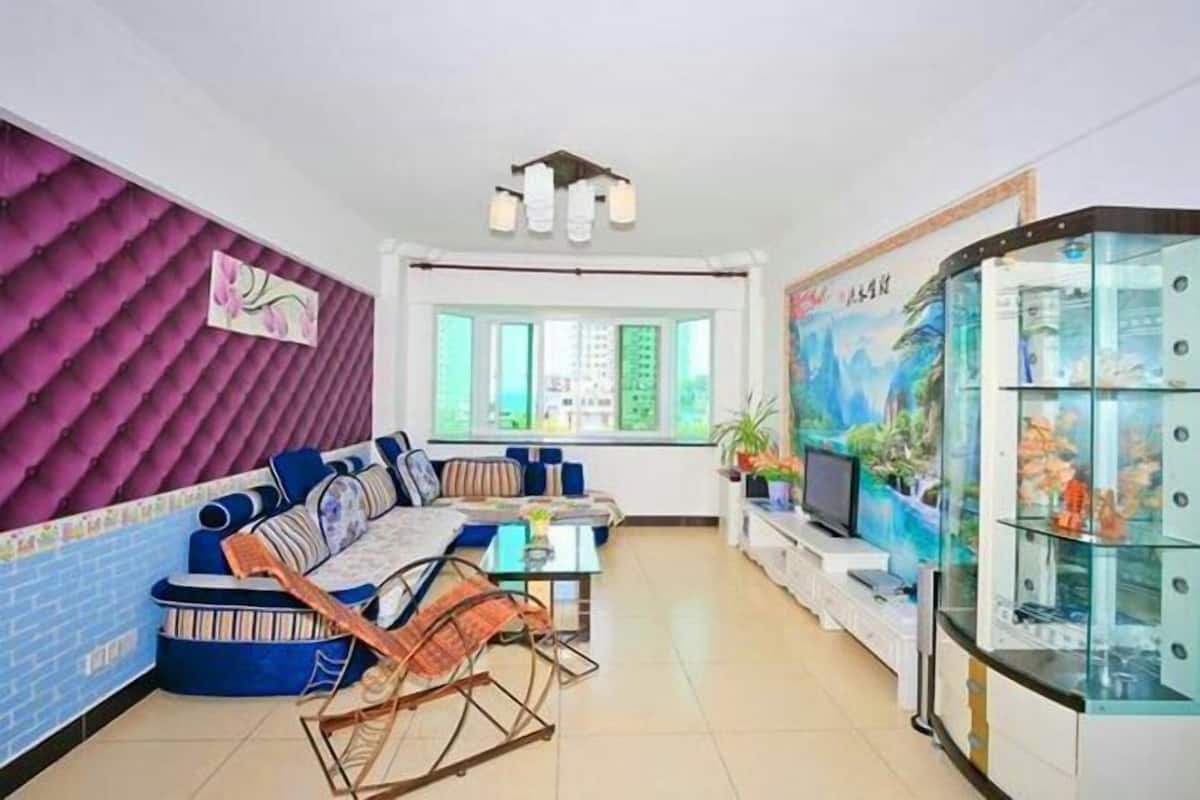 Een woonkamer met een bank, een salontafel en een televisie. Er is een raam met uitzicht op groen.