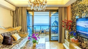 A modern living room with a sofa, a TV, a chandelier, and a view of the sea.