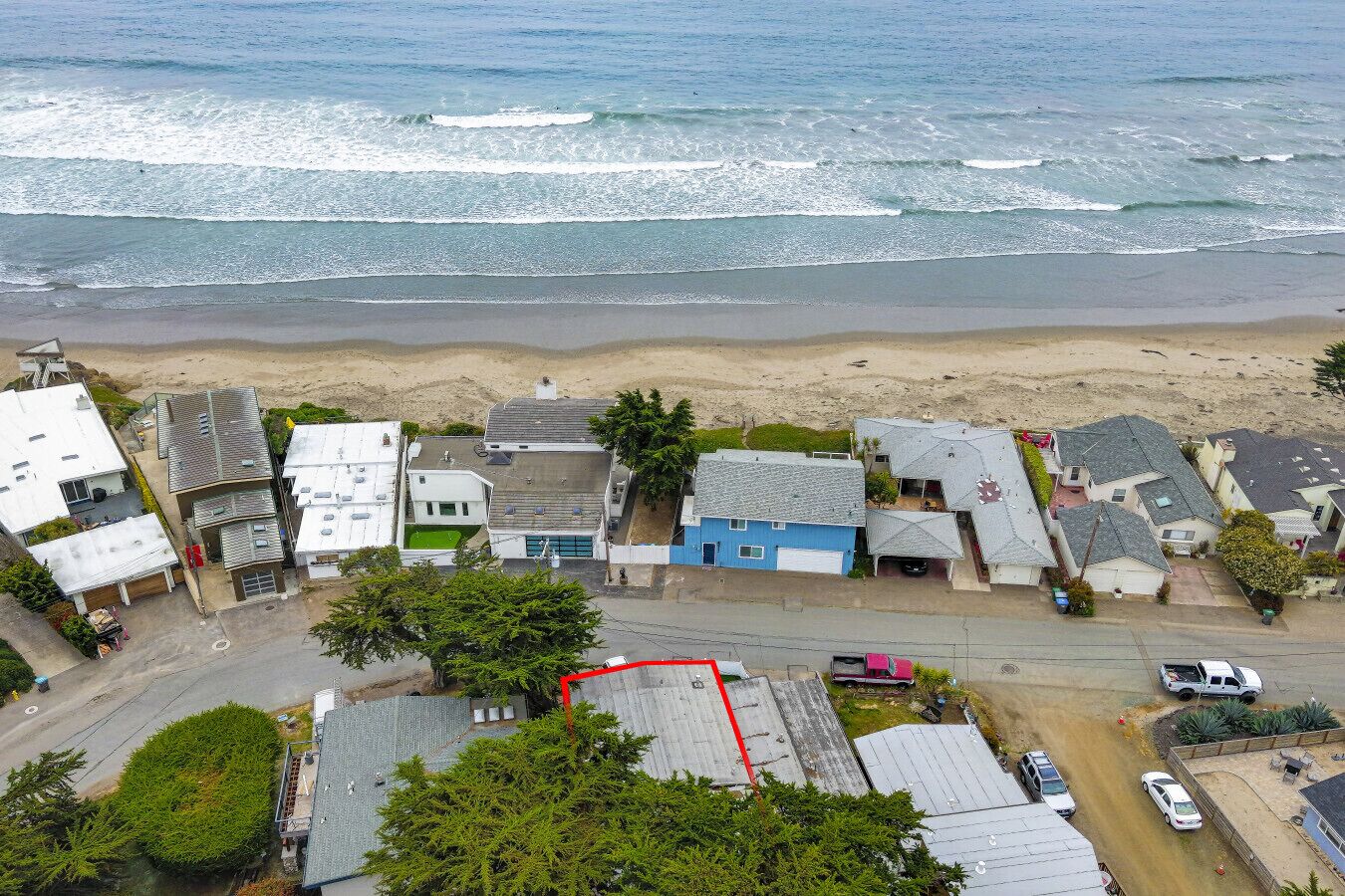 Vista aérea de uma área residencial costeira com casas, uma praia e uma estrada.