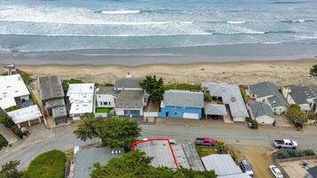 Vista aérea de uma área residencial costeira com casas, uma praia e uma estrada.