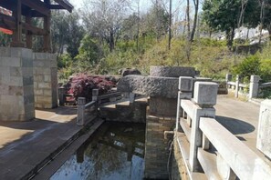 A stone bridge over a small water channel, surrounded by greenery and stone structures. - Red Clay Image Hotel Kunming (Kunming)