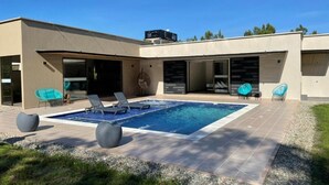 Une maison moderne dotée d’une piscine, d’un espace de détente extérieur et d’un garage.