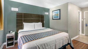 A hotel room with a large bed, a nightstand, a painting on the wall, and a door. - Knights Inn Bristol (Bristol)