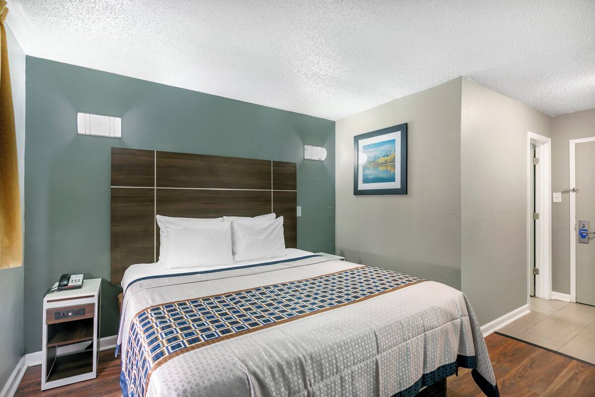 A hotel room with a large bed, a nightstand, a painting on the wall, and a door.