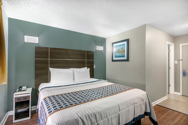 Una habitación de hotel con una cama grande, una mesita de noche, un cuadro en la pared y una puerta.