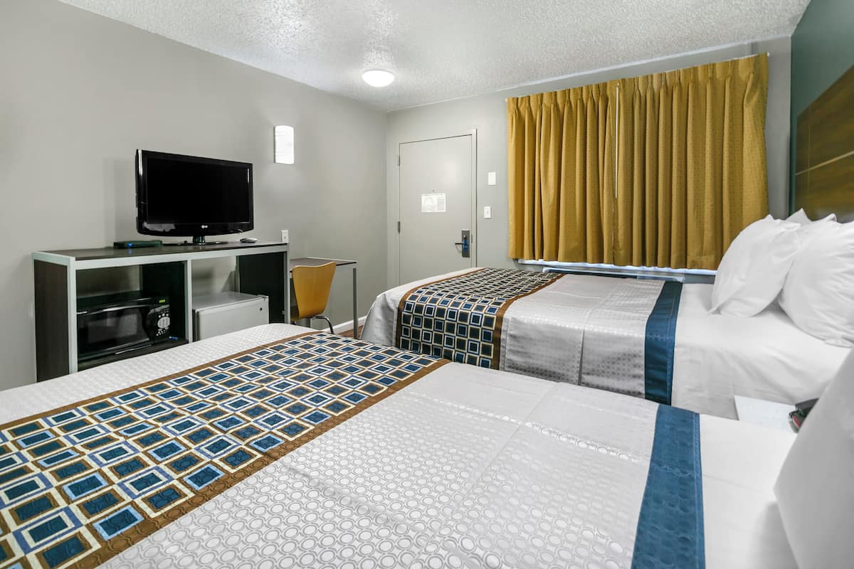 A hotel room with two beds, a TV, a desk with a computer, and a window with curtains.