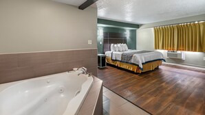 A modern hotel room with a large bathtub, a neatly made bed, and a wooden floor. - Knights Inn Bristol (Bristol)