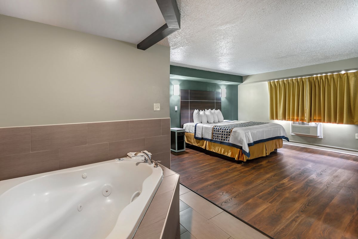 A modern hotel room with a large bathtub, a neatly made bed, and a wooden floor.