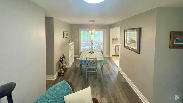 A dining area with a table set for four, a kitchen in the background, and a hallway leading to a door.