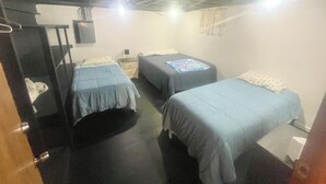 A small, dimly lit room with two single beds, a nightstand, and a desk.