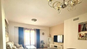 Ein modernes Wohnzimmer mit Essbereich, einer Couch, einem Fernseher und einer Pendelleuchte.