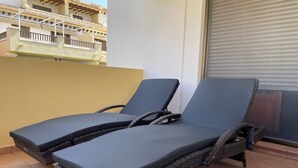 Ein Balkon mit zwei dunklen Liegestühlen und einem Korbstuhl-Tisch.