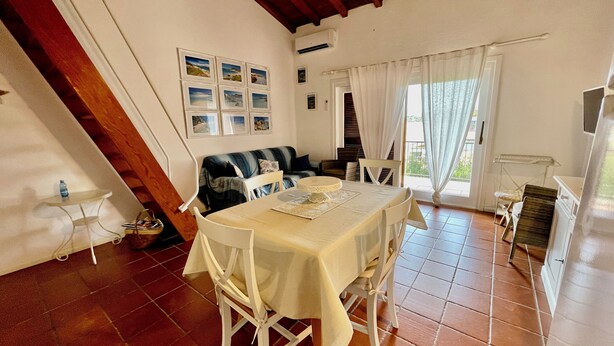 Un coin repas avec une table dressée pour quatre personnes, un canapé et une fenêtre avec des rideaux.