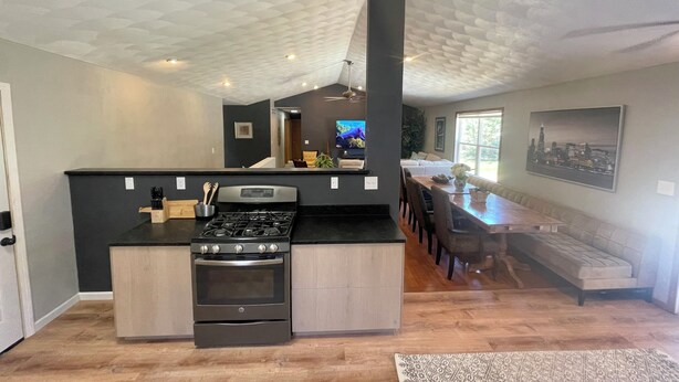 A modern kitchen with a central island, built-in oven, and a dining area with a long table and chairs. - Huge house for large groups! Basketball court, arcade, putting green.4 bathroom (Machesney Park)