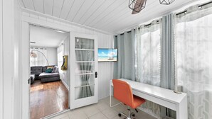 A modern living room with a white desk, orange chair, and a television displaying a beach scene. - Sunny Side Murry Hill Home (Jacksonville)